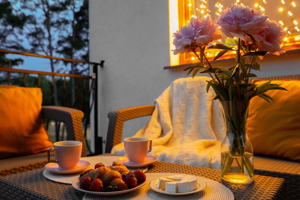 Balkon dekorasyonu. Akşam balkonda, yiyecek, içecek ve çiçeklerle süslenmiş rattan bir masa bulunuyor.