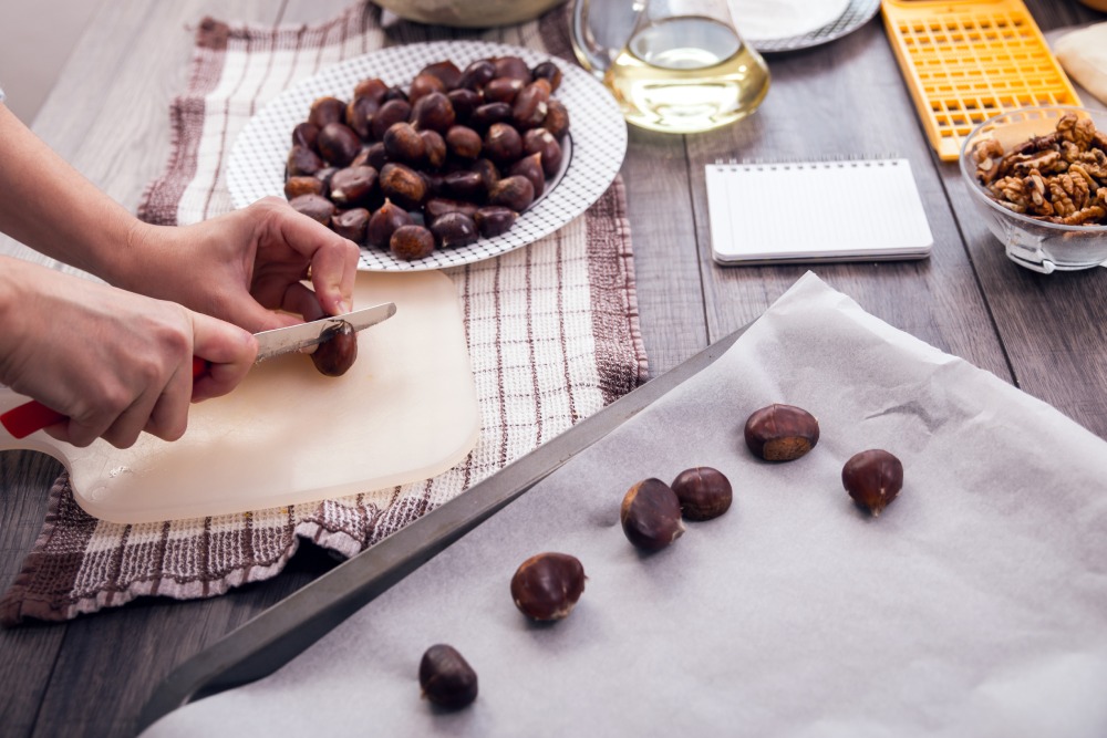 Kadın fırında kestane yapımı için kestaneleri bıçakla çizerek hazırlıyor.
